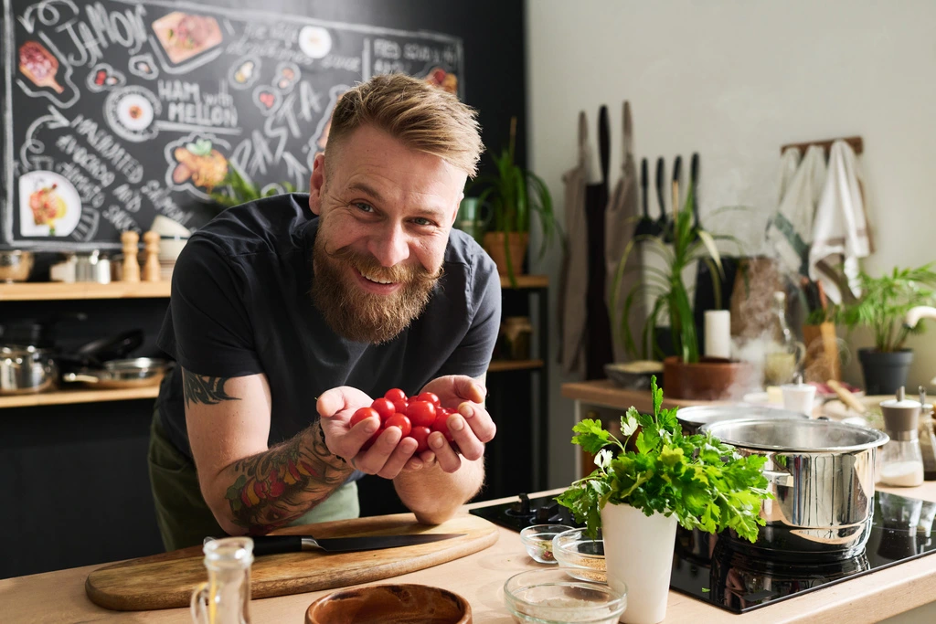Jaxson Riley, creator of the YumDrizzle food blog, smiling warmly at the camera while holding a handful of fresh cherry tomatoes in his kitchen.