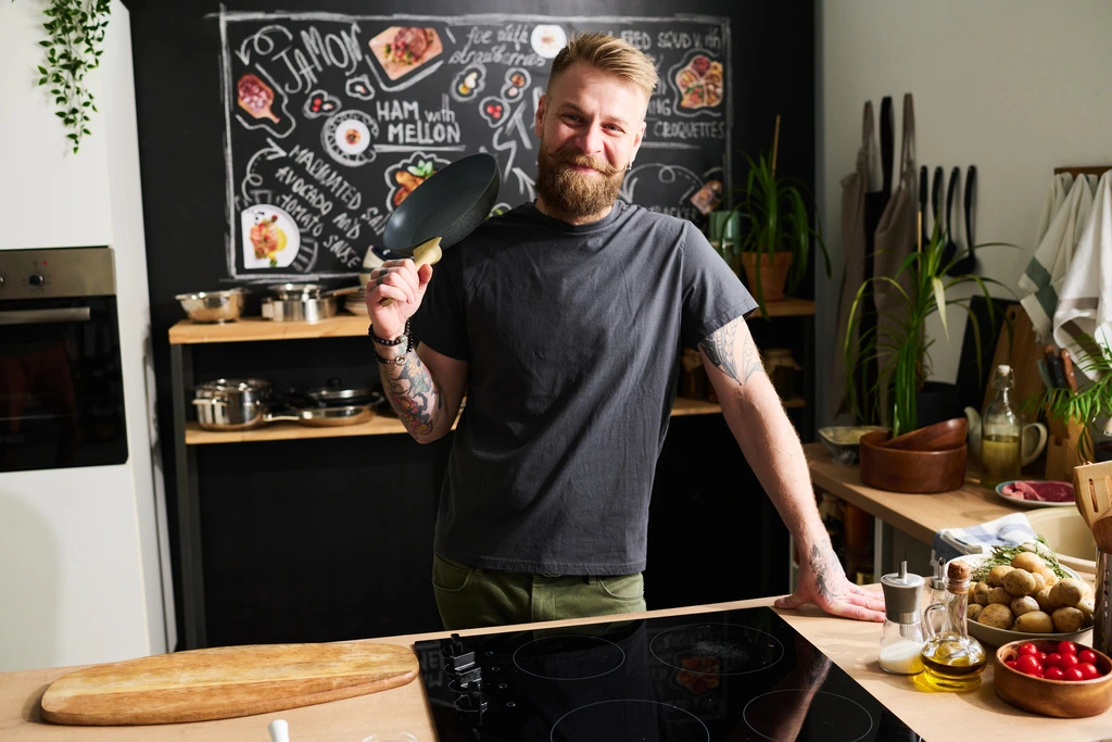 Jaxson Riley, the cook behind YumDrizzle, smiling confidently in his kitchen while holding up a small frying pan, ready to start cooking a simple recipe.