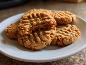 A stack of four classic, fork-pressed peanut butter cookies on a white plate, one cookie is broken open.