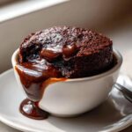 Close-up of a warm chocolate pudding cake with rich sauce oozing over the side of a white ramekin.