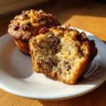 Close-up of a delicious banana nut muffin cut in half showing moist crumb and walnuts on top.
