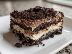 A rich, layered slice of no-bake dirt cake featuring dark chocolate cookie crumbs and creamy filling on a white plate.
