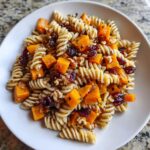 A close-up of amazing fall pasta salad featuring fusilli pasta, roasted butternut squash cubes, dried cranberries, and walnuts.