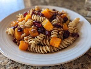 A white bowl filled with amazing fall pasta salad featuring rotini pasta, roasted butternut squash cubes, walnuts, and dried cranberries.