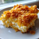 A close-up shot of a creamy slice of hashbrown casserole topped with golden, crunchy cornflakes.