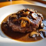 A close-up of a perfectly cooked salisbury steak smothered in rich mushroom gravy and sliced mushrooms.