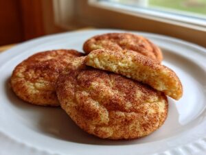 Close-up of three freshly baked Snickerdoodle cookies, one broken in half showing the soft interior, dusted with cinnamon sugar.