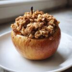 A single, golden baked apples dessert topped generously with a cinnamon oat crumble.
