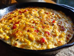 Close-up of hot, baked corn dip with cream cheese, featuring yellow corn kernels and red peppers in a cast iron skillet.