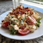 A scoop of creamy blt chicken salad mixed with lettuce and topped with crispy bacon bits and halved cherry tomatoes.