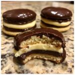 A close-up of one of the boston cream pie cookies with a bite taken out, showing vanilla cream filling and chocolate glaze.