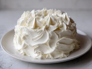 A small, round cake entirely covered in thick, swirled peaks of homemade cream cheese frosting.