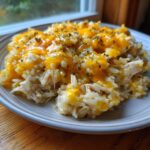 A close-up serving of cheesy chicken and rice topped with melted orange cheddar cheese and dried herbs.