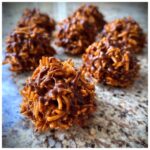 A close-up of a freshly made haystack cookie drizzled with melted chocolate, resting on a granite counter.