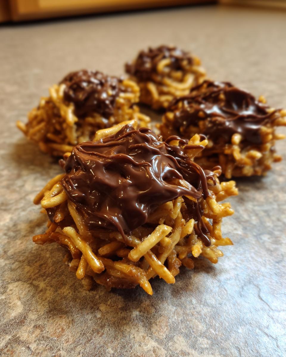 Four homemade haystack cookies topped with melted chocolate, sitting on a speckled countertop.