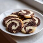 A plate of freshly baked chocolate and vanilla pinwheel cookies showing distinct dark brown and light dough swirls.