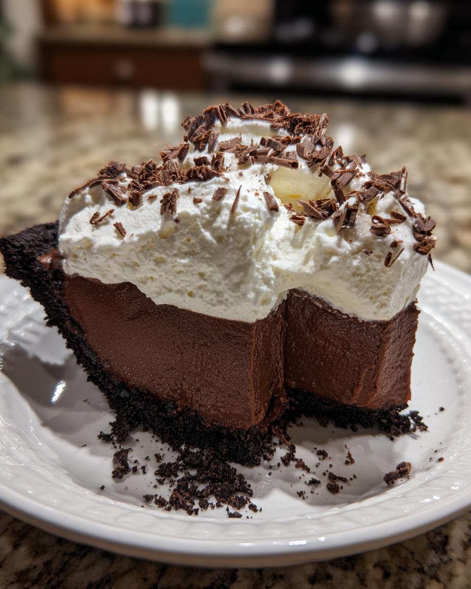 A decadent slice of Christmas chocolate cream pie featuring a dark chocolate filling, cookie crust, and topped with whipped cream and chocolate shavings.