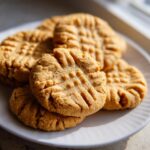 A stack of golden brown peanut butter cookies with classic fork crosshatch marks, served on a white plate.