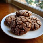 A plate of four dark, cracked gingersnap cookies heavily coated in sparkling white sugar crystals.