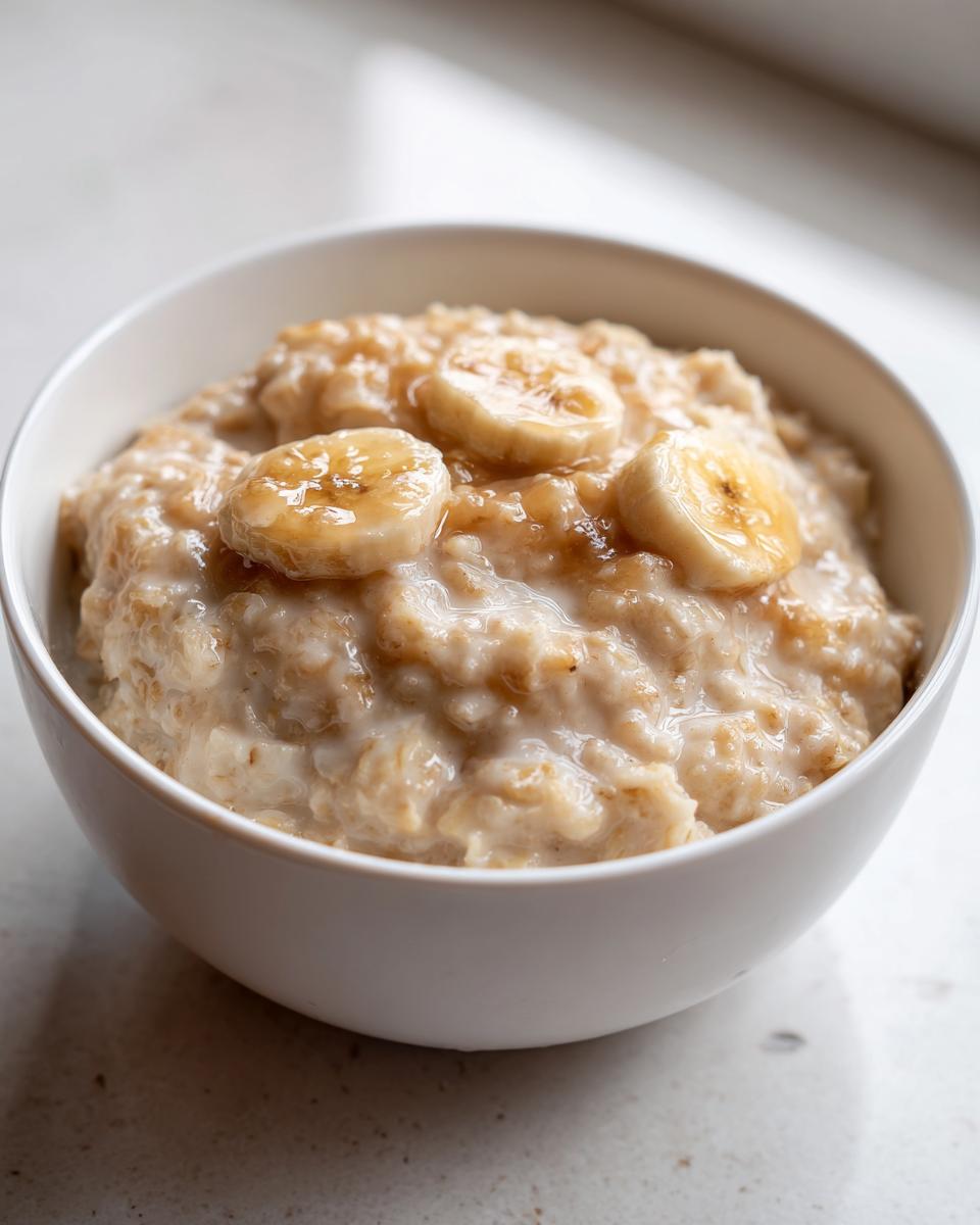 A close-up of a white bowl filled with creamy banana oatmeal, topped with caramelized banana slices.
