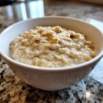A close-up of creamy banana oatmeal served in a white bowl on a granite countertop.