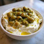 Close-up of a creamy white dirty martini dip topped generously with green olives and olive oil.