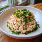 A large mound of creamy salmon dip garnished heavily with fresh dill and lemon zest in a white bowl.