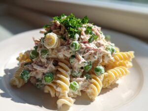 A mound of creamy tuna pasta salad featuring fusilli pasta, green peas, and topped with fresh parsley.