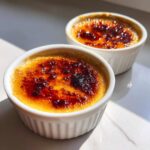 Two servings of homemade Creme Brulee in white ramekins, featuring a dark, crackling caramelized sugar top.