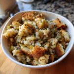 Close-up of a white bowl filled with savory crock pot stuffing, featuring bread cubes, celery, onions, and fresh thyme.