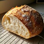 A rustic, freshly baked Italian bread loaf, cut in half to show the airy crumb, resting on a wire cooling rack.