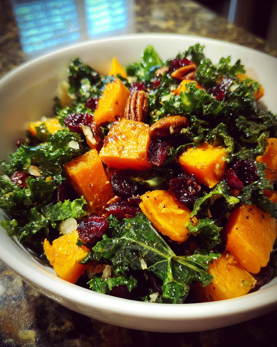 Close-up of a vibrant Fall Harvest Salad featuring kale, roasted orange squash cubes, pecans, and dried cranberries.