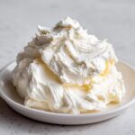 A generous, fluffy swirl of white cream cheese frosting piled high on a small white dish.