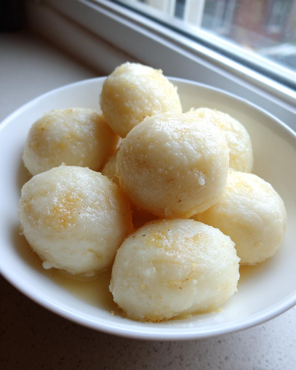 A close-up of several fluffy potato dumplings resting in a white bowl with a small amount of melted butter.