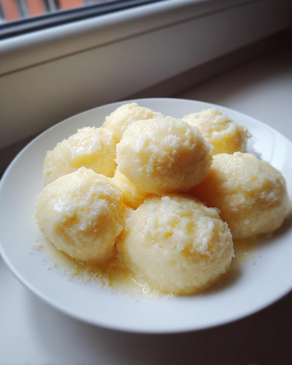 A plate of freshly made, fluffy potato dumplings topped with melted butter and grated cheese.