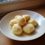 A white plate holding several fluffy potato dumplings dusted with sweet crumbs and butter.