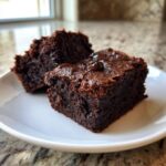 Close-up of two rich, dark chocolate sweet potato brownies topped with melted chocolate chips on a white plate.