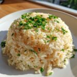 A perfectly molded serving of fluffy garlic butter rice topped with fresh chopped parsley.