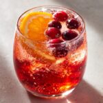 Close-up of a glass filled with sparkling red thanksgiving punch, garnished with fresh cranberries and an orange slice.