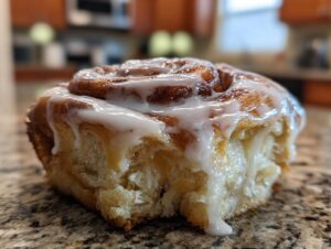 A close-up, mouth-watering shot of a single, fluffy cinnamon roll topped with thick white icing.