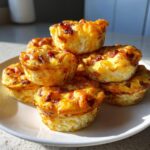 A stack of freshly baked, golden brown bacon egg bites piled high on a white plate.