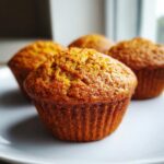 A close-up, appetizing photo of golden brown sweet potato muffins resting on a white plate.
