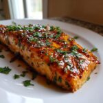 Close-up of a perfectly cooked salmon fillet glazed with honey garlic sauce and topped with fresh chopped parsley.