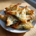 A close-up of golden, flaky Mediterranean Spinach and Feta Cheese Crisps stacked on a white plate.