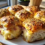 Close-up of baked Ham and Cheese Sliders with gooey melted cheese oozing out, topped with poppy seeds.