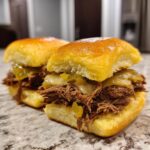 Two delicious Mississippi pot roast sliders stacked high with shredded beef, melted cheese, and pepperoncini on shiny brioche buns.