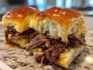 Two halves of a juicy mississippi pot roast sliders showing shredded beef, melted cheese, and glossy buns.