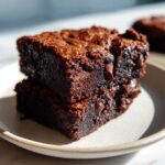 Two stacked, fudgy black bean brownies with visible chocolate chips, sitting on a light ceramic plate.