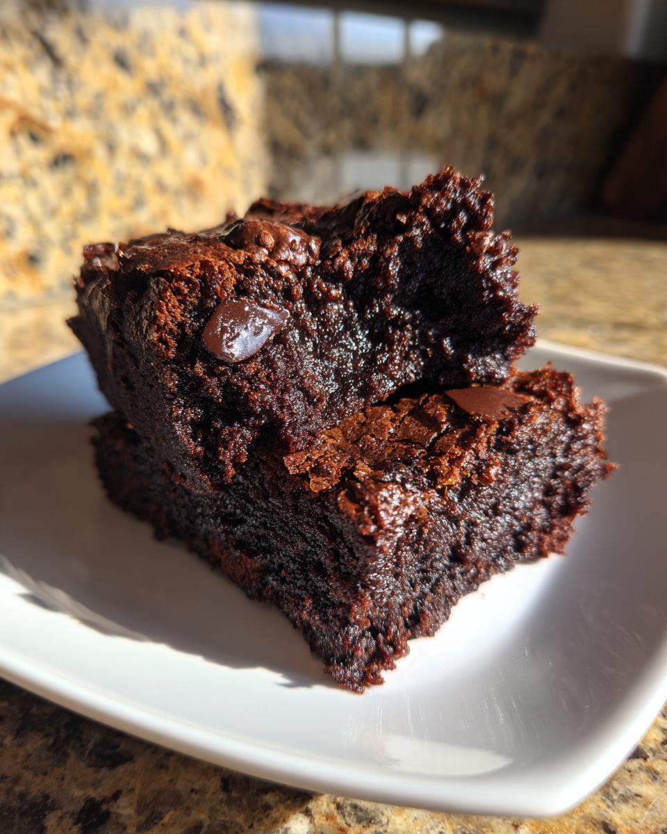 Two rich, fudgy pieces of sweet potato brownies stacked on a small white plate, showing melted chocolate chips.