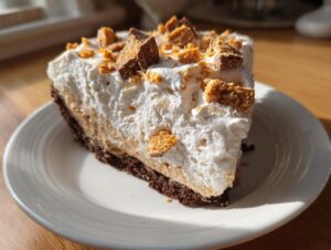 A tempting slice of no-bake butterfinger pie featuring a chocolate crust, creamy filling, and whipped topping sprinkled with candy pieces.